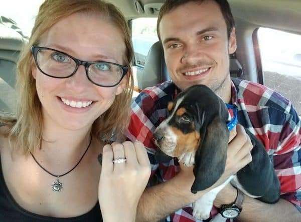 Happy couple posing with their adopted basset hound and new engagement ring