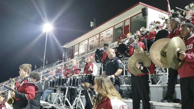 Police Officer Jams With The School Band In The Stands At Football Game