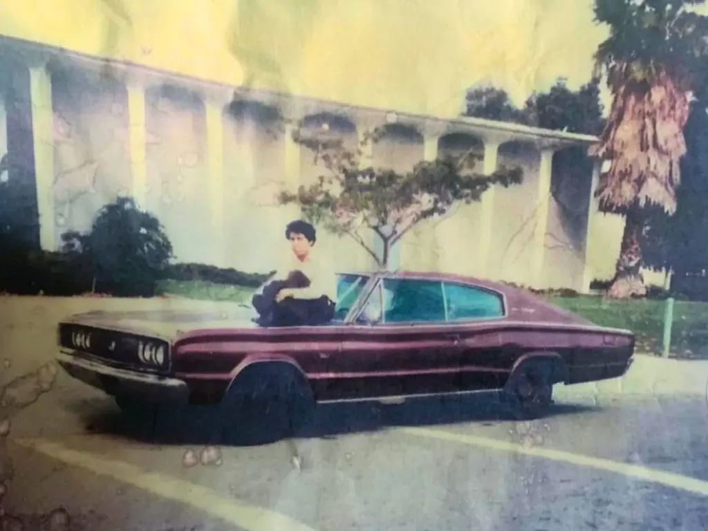 A man sat on the bonnet of a 1968 Dodge Charger.