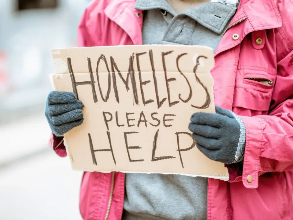 A homeless person holding a sign saying homless please help.