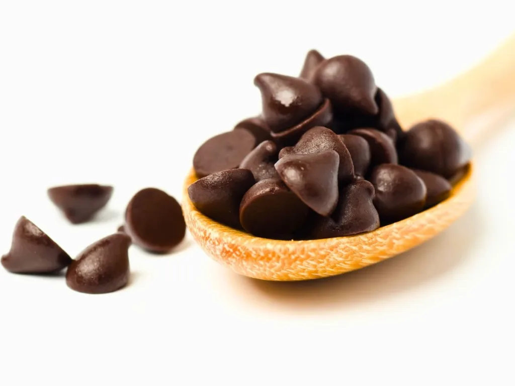 A wooden spoon filled with dark chocolate chips, with some scattered around.