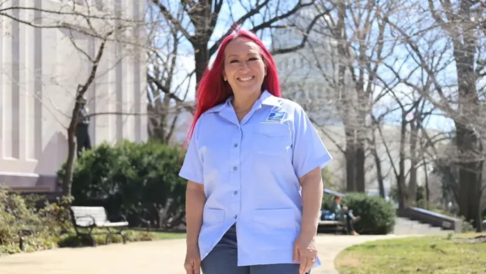 Postal worker Rungphet Bodnar smiling in her postal uniform outdoors on a sunny day.