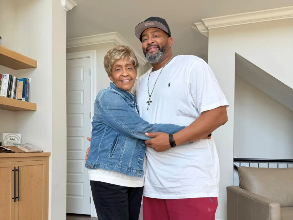 Reunited mother and son smile and embrace while posing together for a photo indoors.