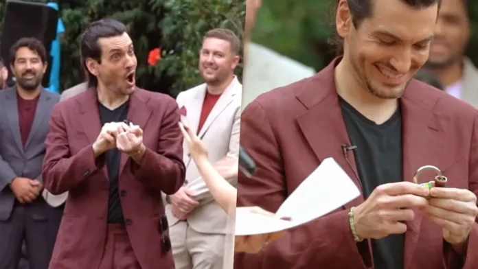Groom in a maroon suit looking shocked and excited as he holds a lock at the altar during a wedding, with smiling guests in the background.