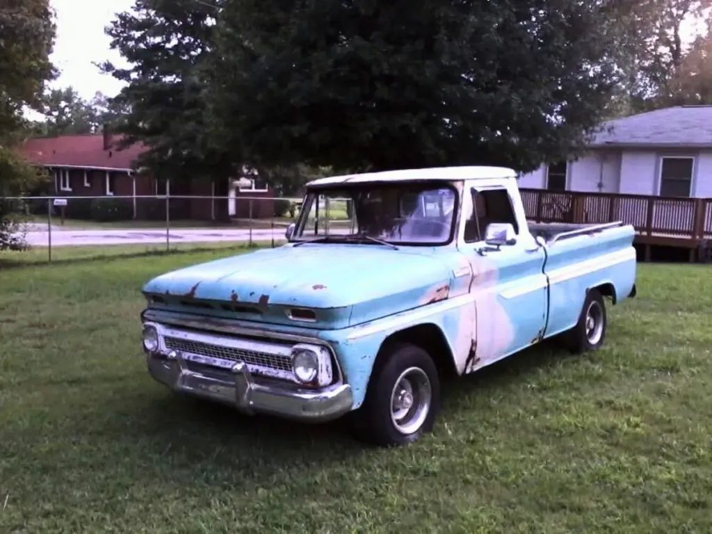 A recent photo of the aged, slightly rusted blue and white Chevy C10 truck parked on grass outside a home.