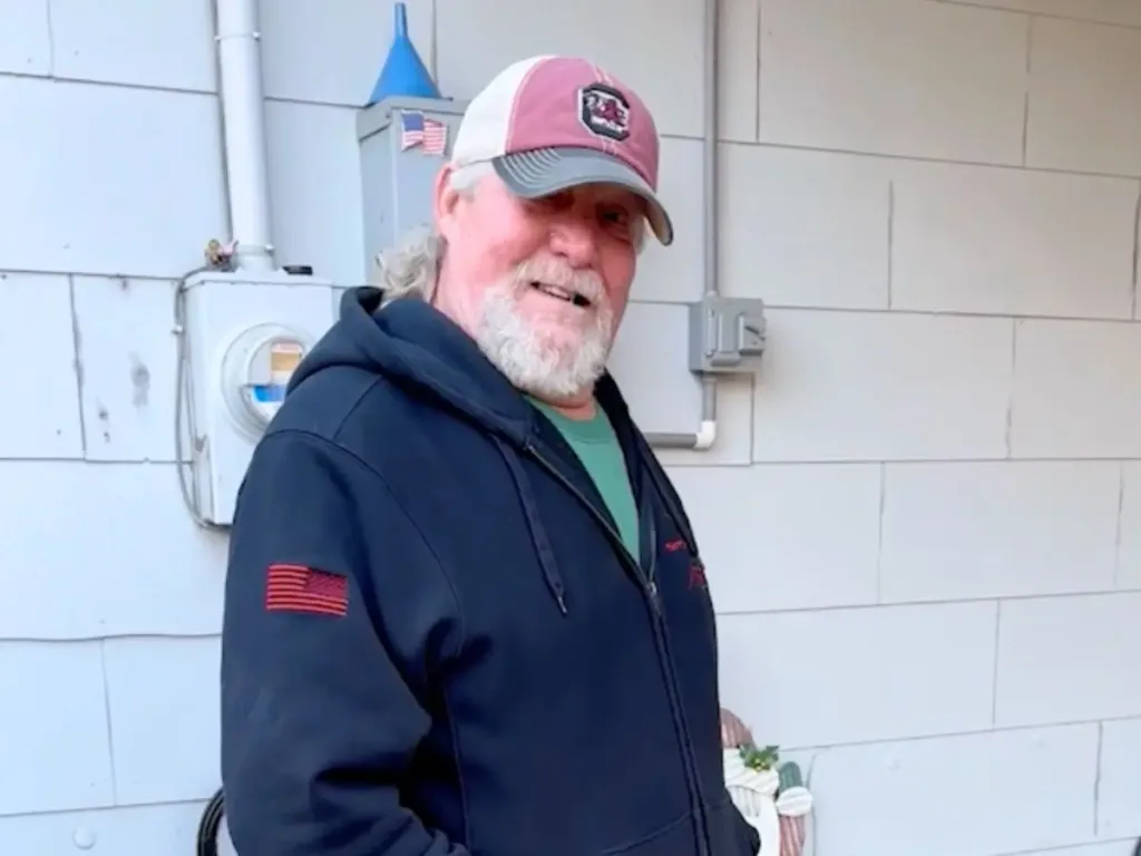 Donnie Couch wearing a cap and smiling warmly, standing outside his home.