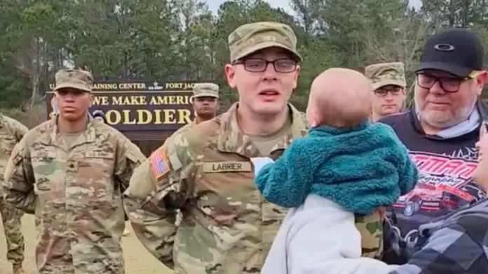 A young soldier stands emotionally surprised as he sees his baby daughter being brought toward him during his boot camp graduation ceremony.