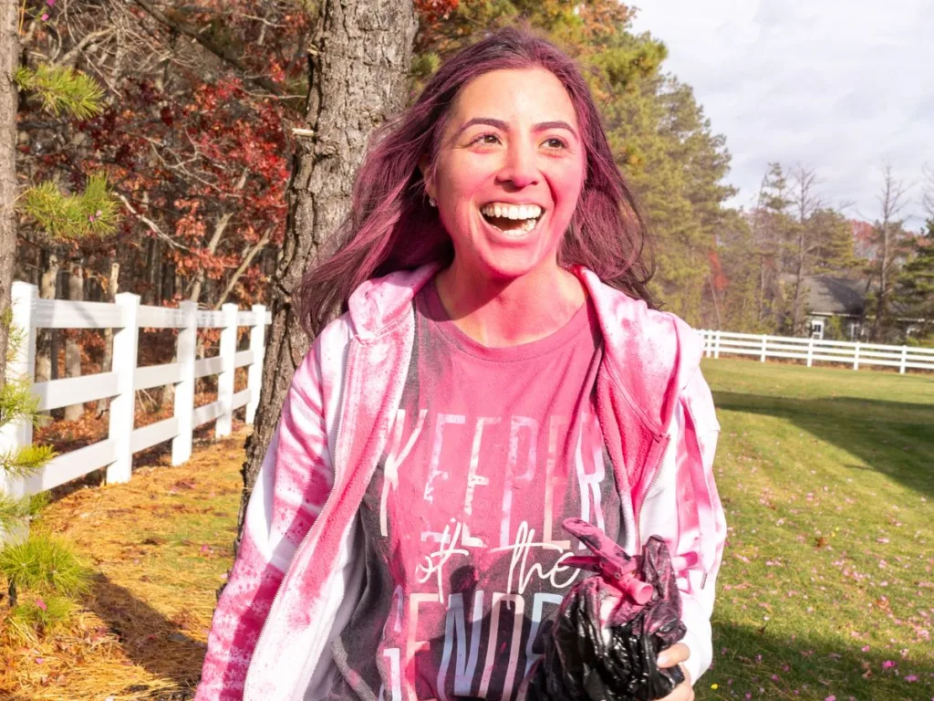 Smiling woman with pink powder on face walking through a field after gender reveal