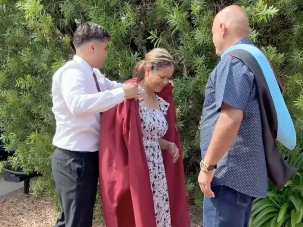 Martin Jr. drapes his graduation gown over his mother while his father, wearing the hood, stands nearby.