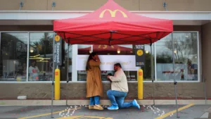 Man proposing to his girlfriend under a McDonald’s tent decorated with candles and petals.