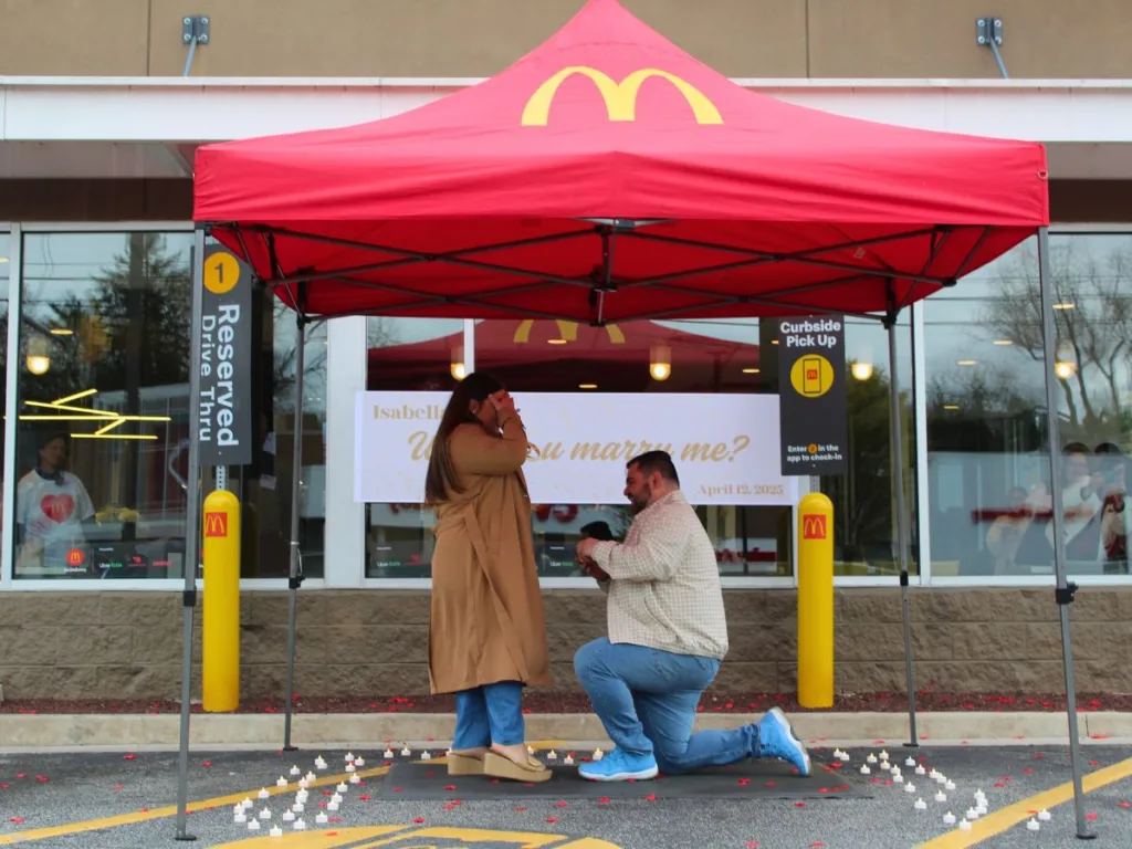 Man proposing to his girlfriend under a McDonald’s tent decorated with candles and petals.