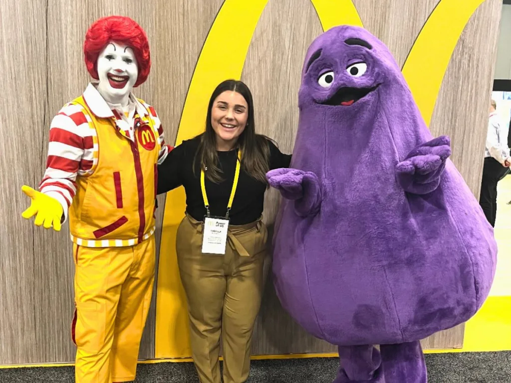 Woman standing between McDonald’s characters Ronald McDonald and Grimace.