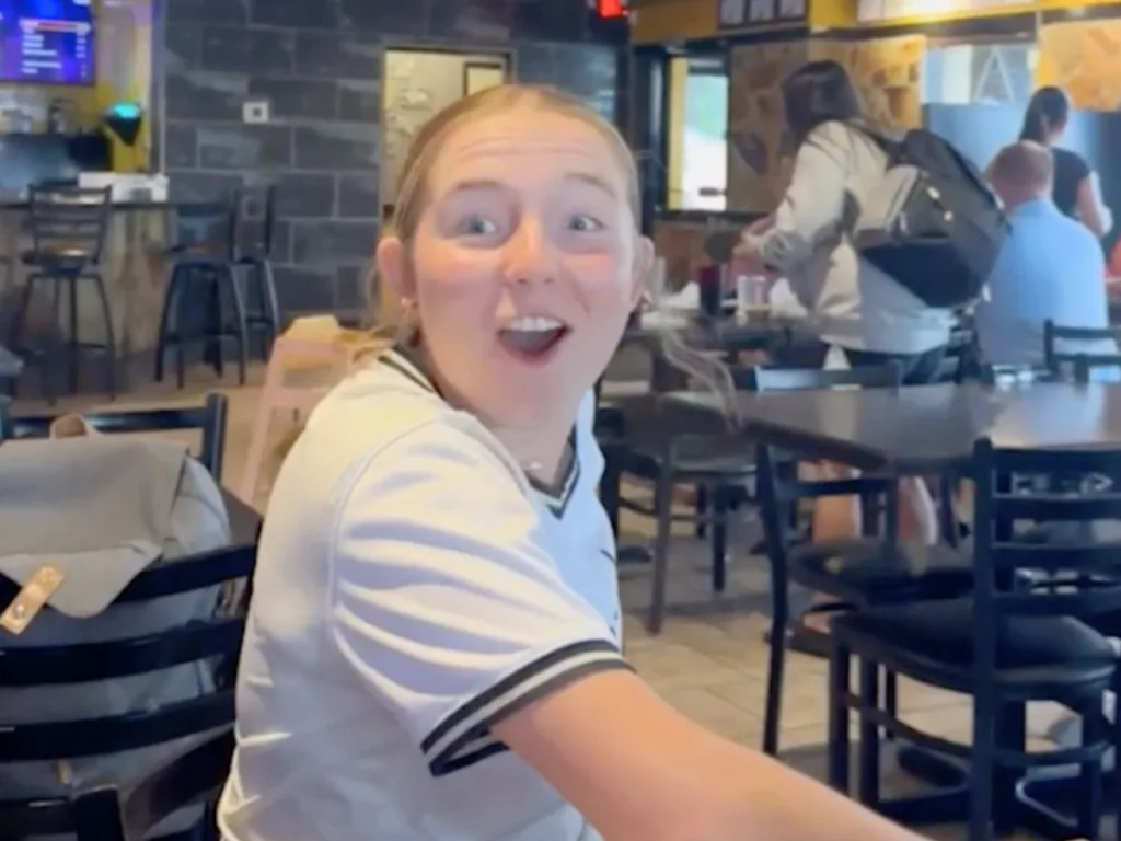 Teen girl looks shocked with joy as she spots her Navy brother entering the restaurant.