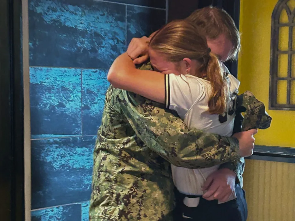 Navy sailor and teen sister embrace tightly in a heartfelt reunion.