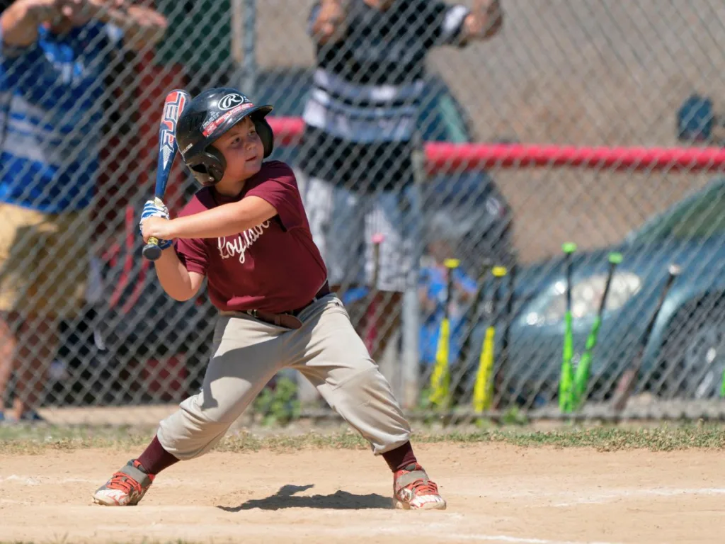 Young boy in a maroon team jersey prepares to swing a baseball bat during a game.