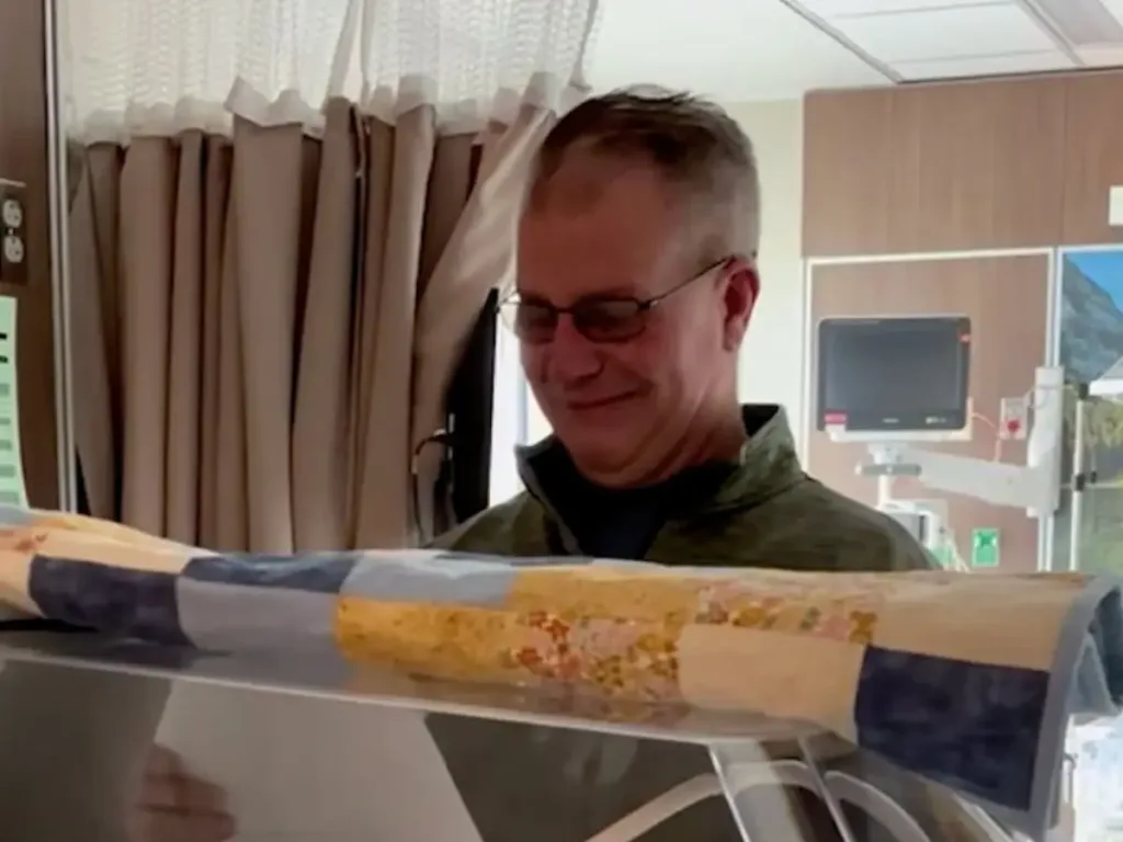 Stepdad Larry stands beside a hospital bassinet, visibly emotional as he reads a name card.