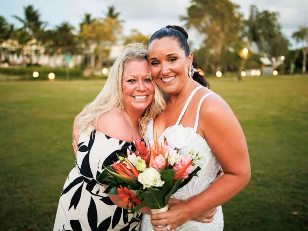 Bride and best friend smiling arm-in-arm on the resort lawn during wedding day.