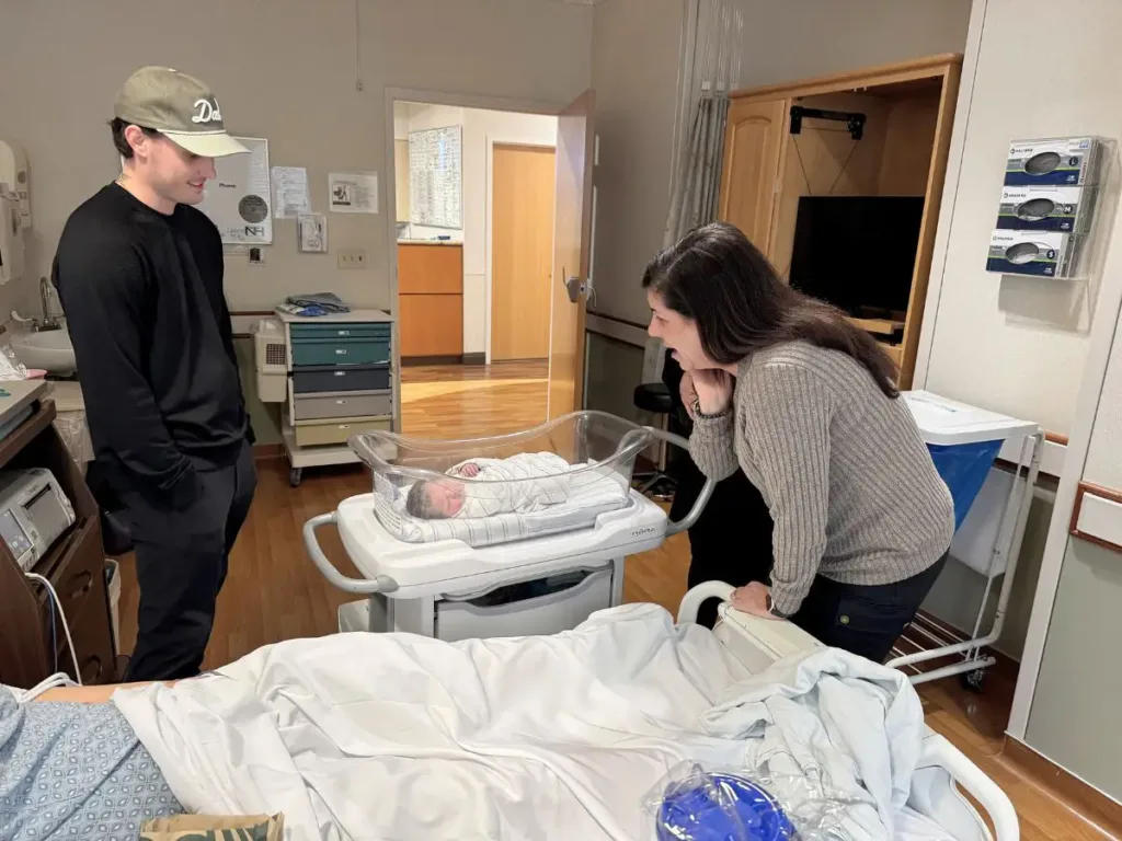 Jimmy stands beside baby Monroe’s bassinet while Natalie leans in to admire her first grandchild in the hospital room.