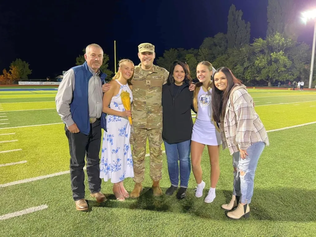Family photo with soldier and homecoming queen nominee on football field.
