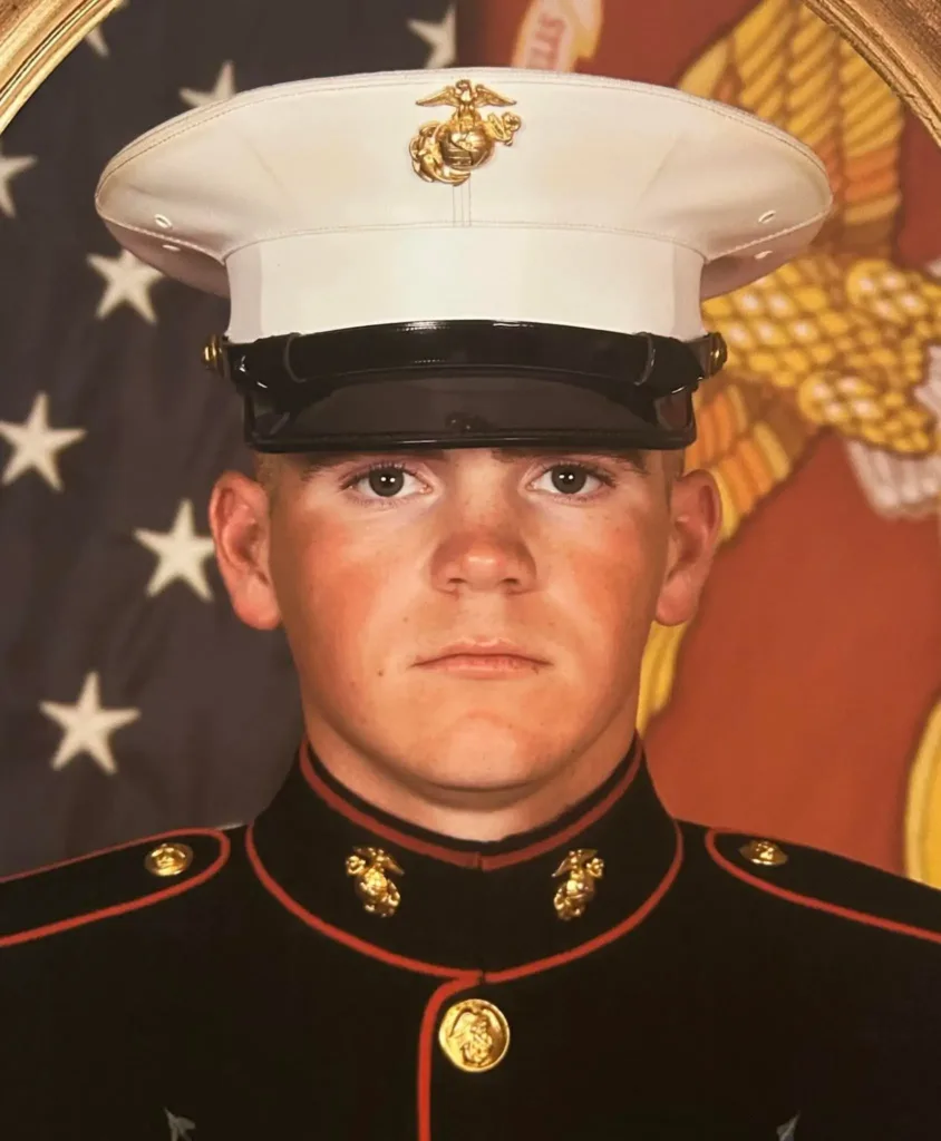 A formal portrait of Marine Brandon Orsi in full dress uniform standing in front of the U.S. flag.