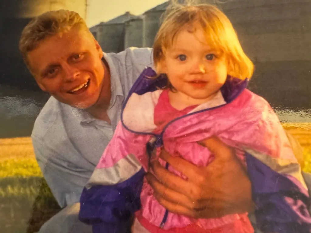 A young Brad holding his stepdaughter Haley as a toddler in a pink jacket.
