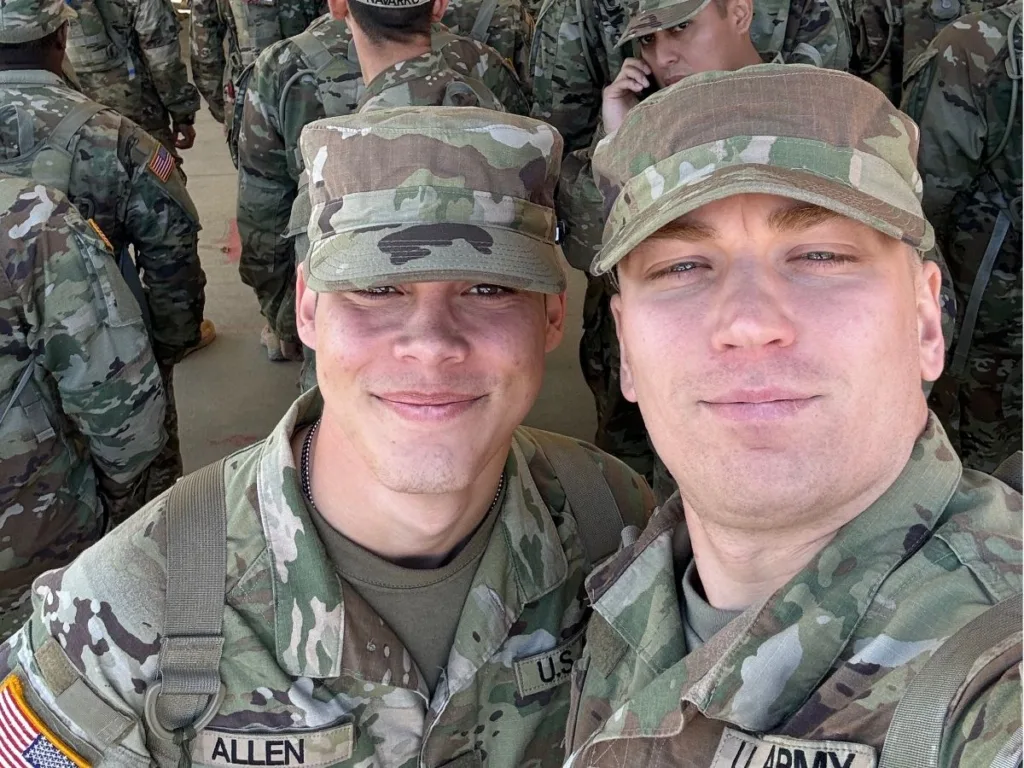 Two uniformed soldiers take a close-up selfie amid a crowd of fellow trainees.