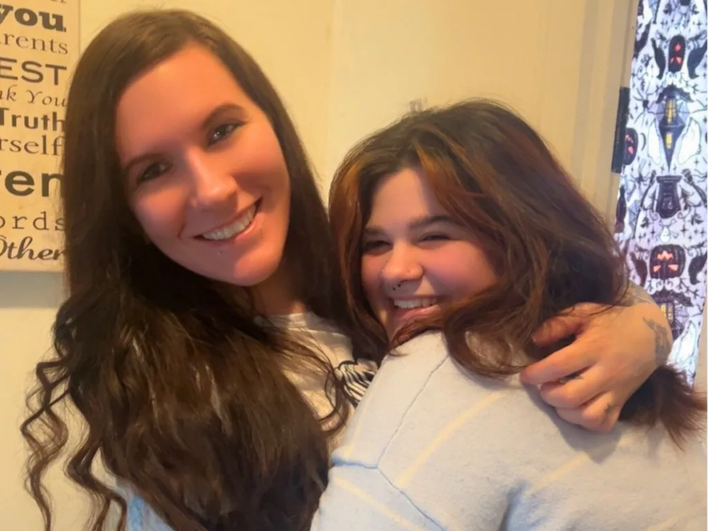 Adoptive mom and teen daughter smile and hug closely at home.