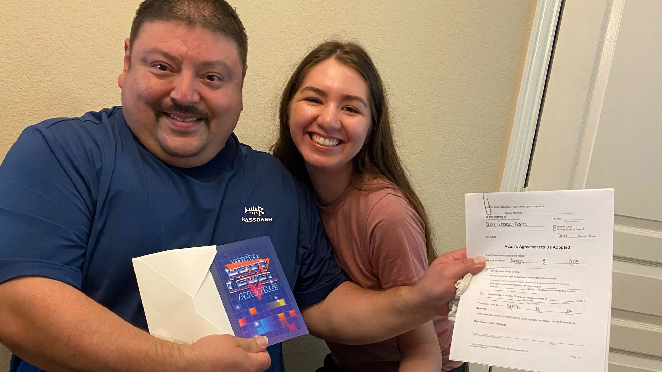 Esteban Steven Lopez and stepdaughter Daisy Garcia smile while holding adult adoption papers and Father's Day card in Houston Texas.