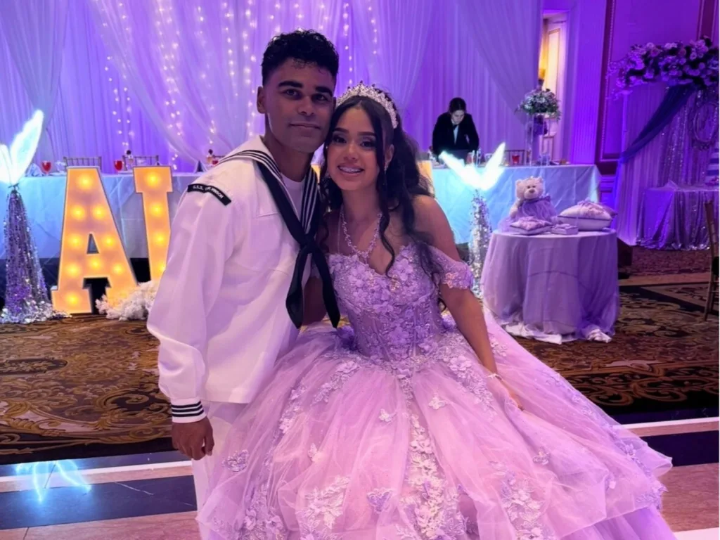 Chris poses beside Alexa in her purple quinceañera dress and tiara at the reception venue.