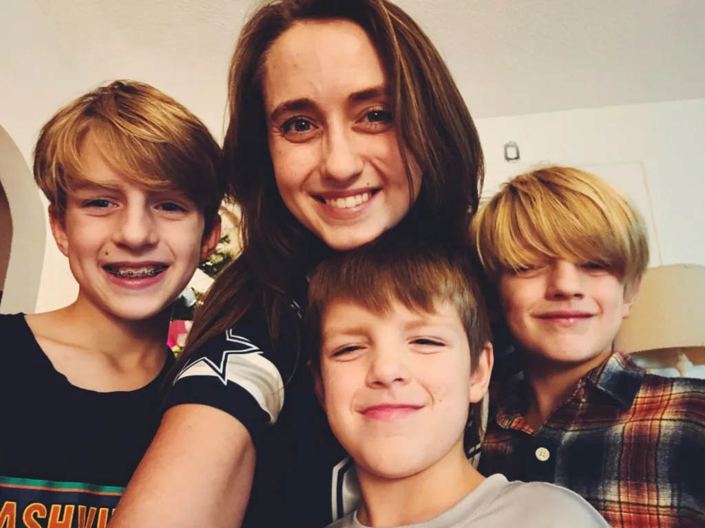 A smiling woman takes a selfie with three boys gathered close beside her.