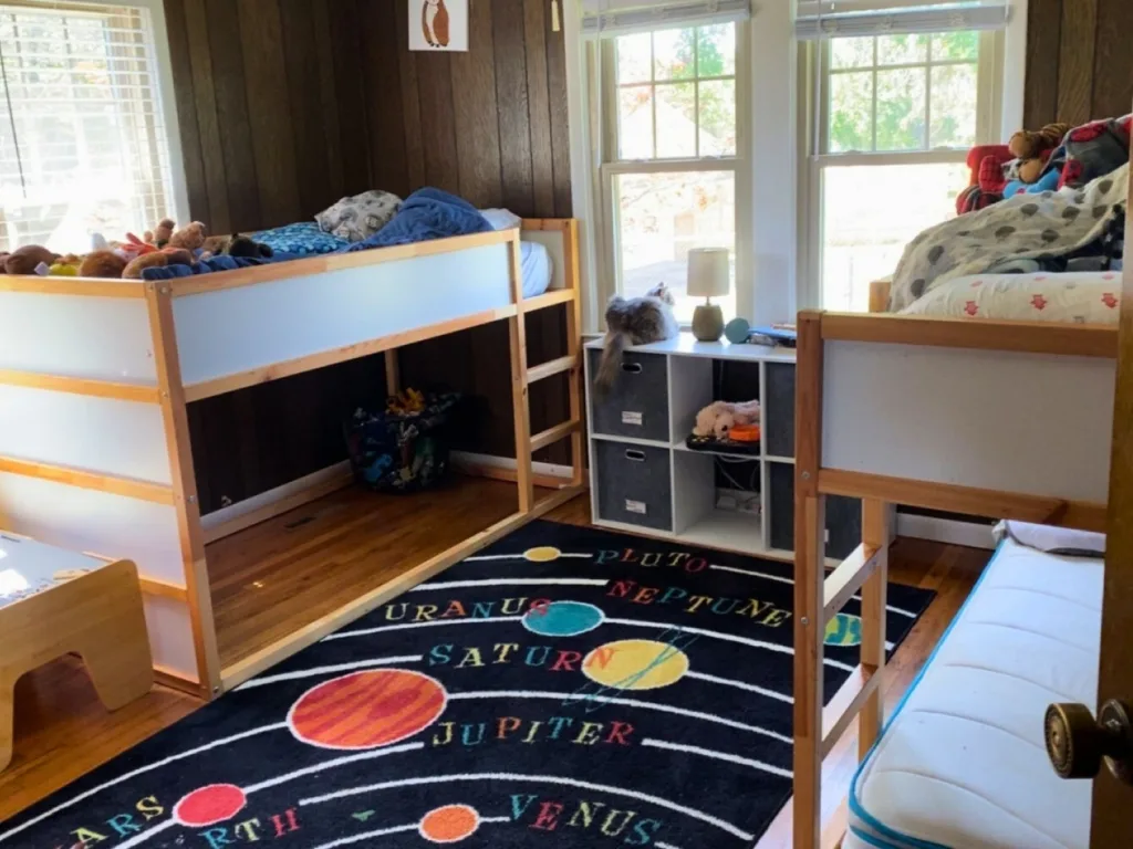 A kids’ bedroom with bunk beds, a twin bed, and a colorful solar system rug.