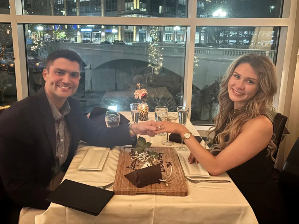 Will holds Emrie’s hand across the table as she shows off her engagement ring.