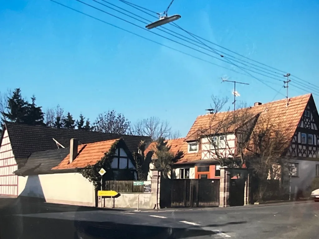 Street view of traditional farmhouse buildings with red tile roofs and half-timbered walls under a blue sky.