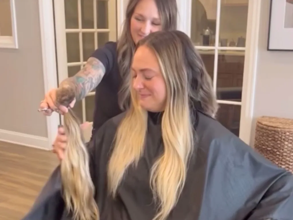 A hairstylist holds up Brooke’s freshly cut long hair as Brooke sits in a salon chair.