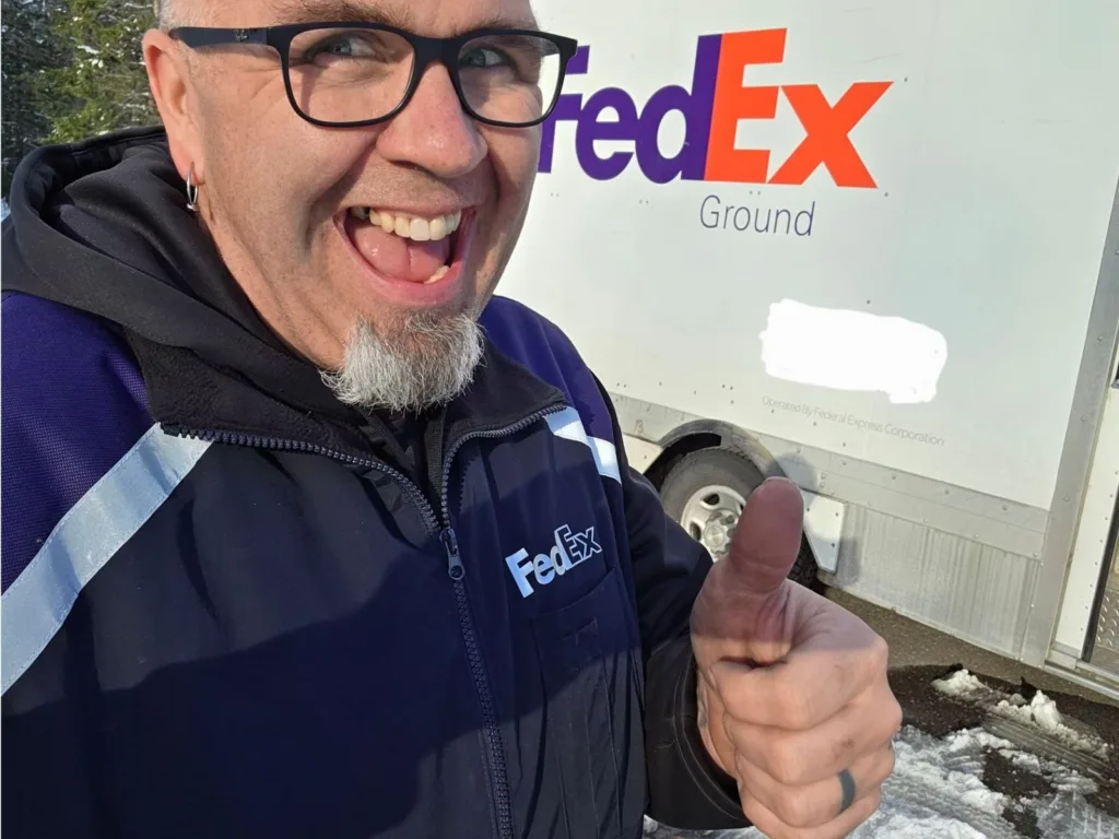 Phil gives a thumbs-up while wearing a FedEx jacket in front of a FedEx Ground truck.