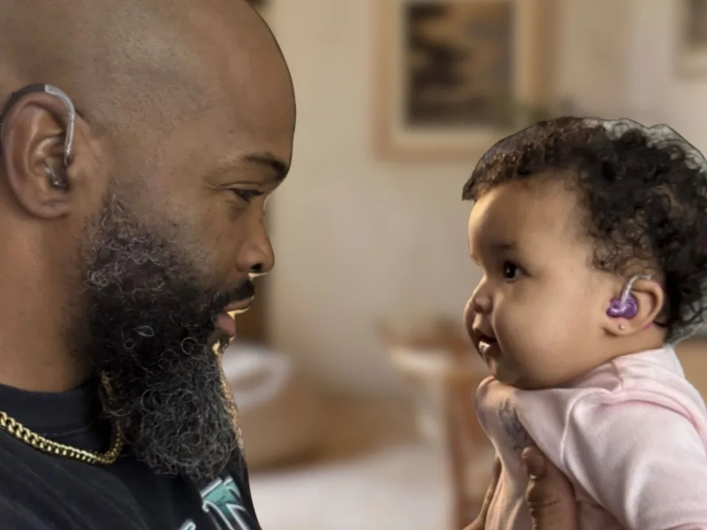 DeMarcus holds Tanaya close as they look at each other, with Tanaya wearing purple hearing aids.