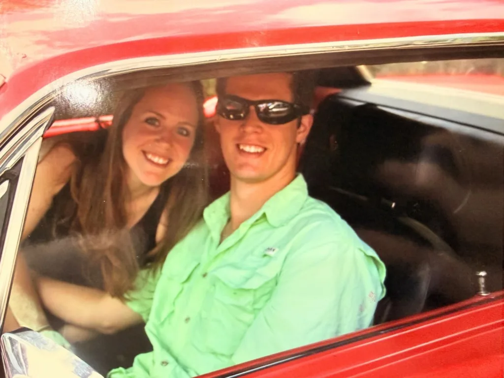 yle and Kalli smile from inside a red classic Mustang, sitting together in the front seats.