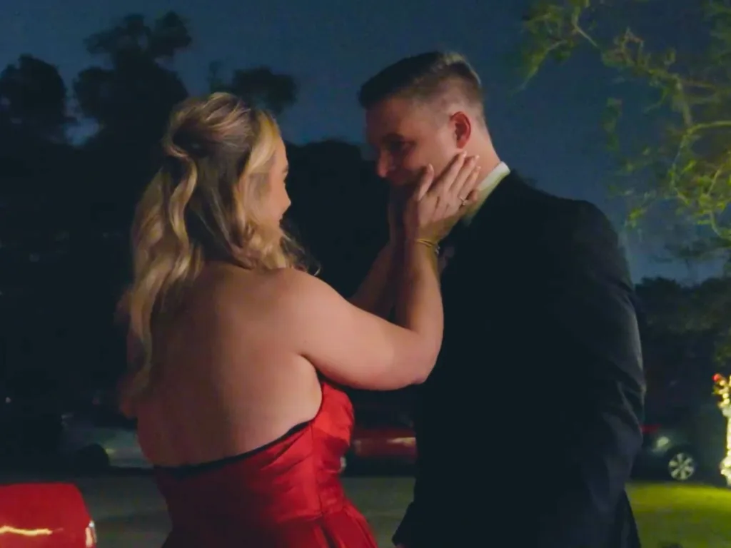 Kalli cups Kyle’s face as they share an emotional moment outdoors at night.