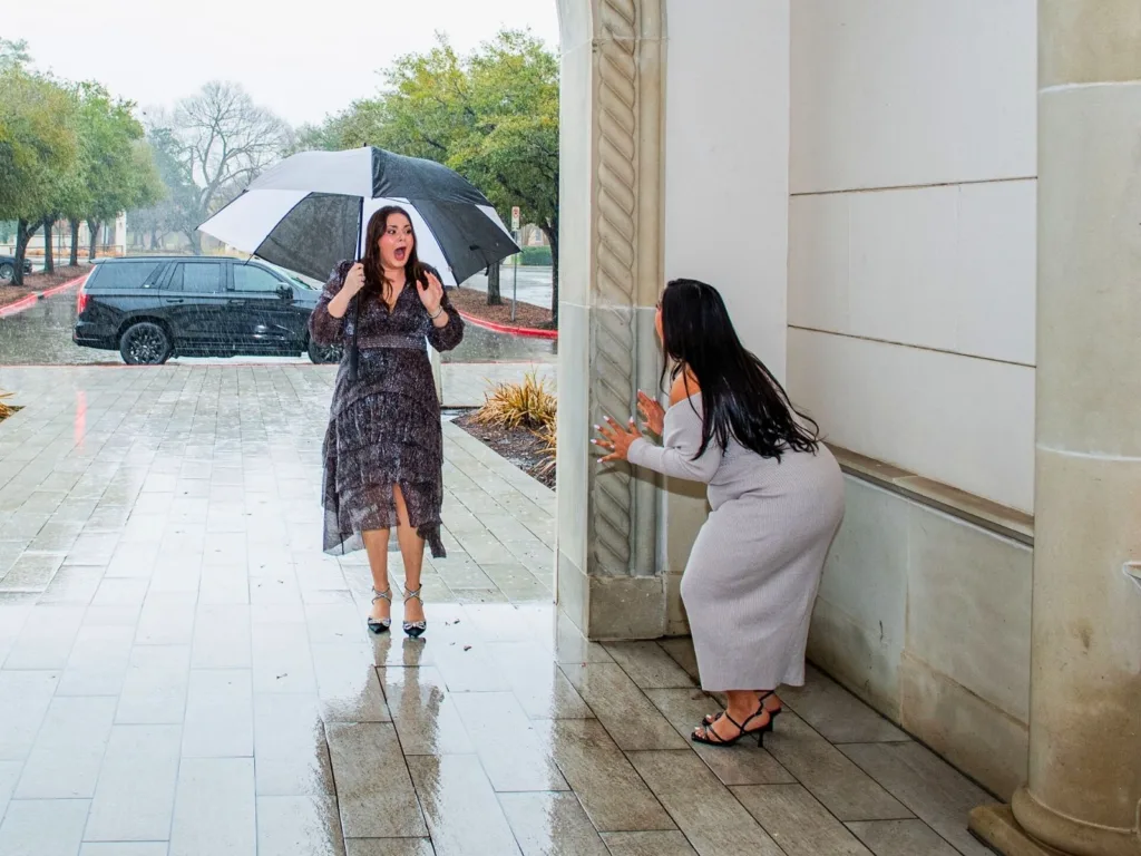 Kim holds an umbrella and looks stunned as a friend waits nearby in the rain.