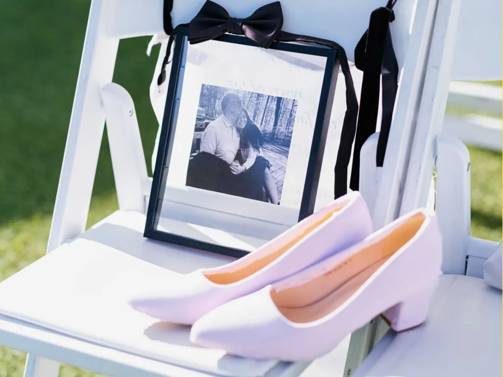 Close-up of a pair of light-colored wedding heels on a white chair beside a framed black-and-white photo tied with a black ribbon.