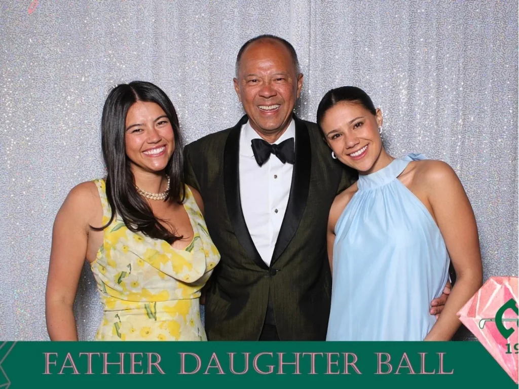 A younger Rodney crouches between Violet and Kendra at a father-daughter dance as all three smile for the camera.