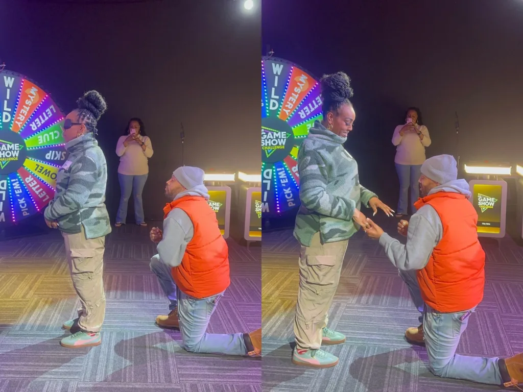 Andre kneels on one knee beside Alicia during a game show experience as she turns toward him.