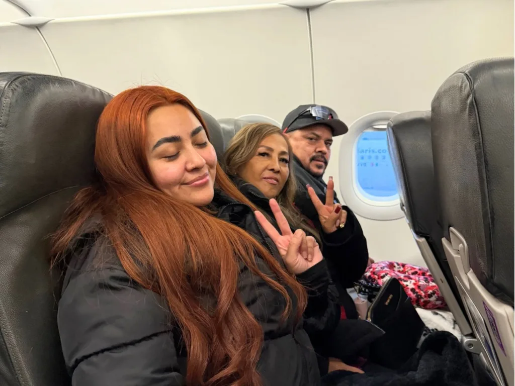 Itsy, Rosa, and Hugo sit together on an airplane, smiling during their trip to visit family.