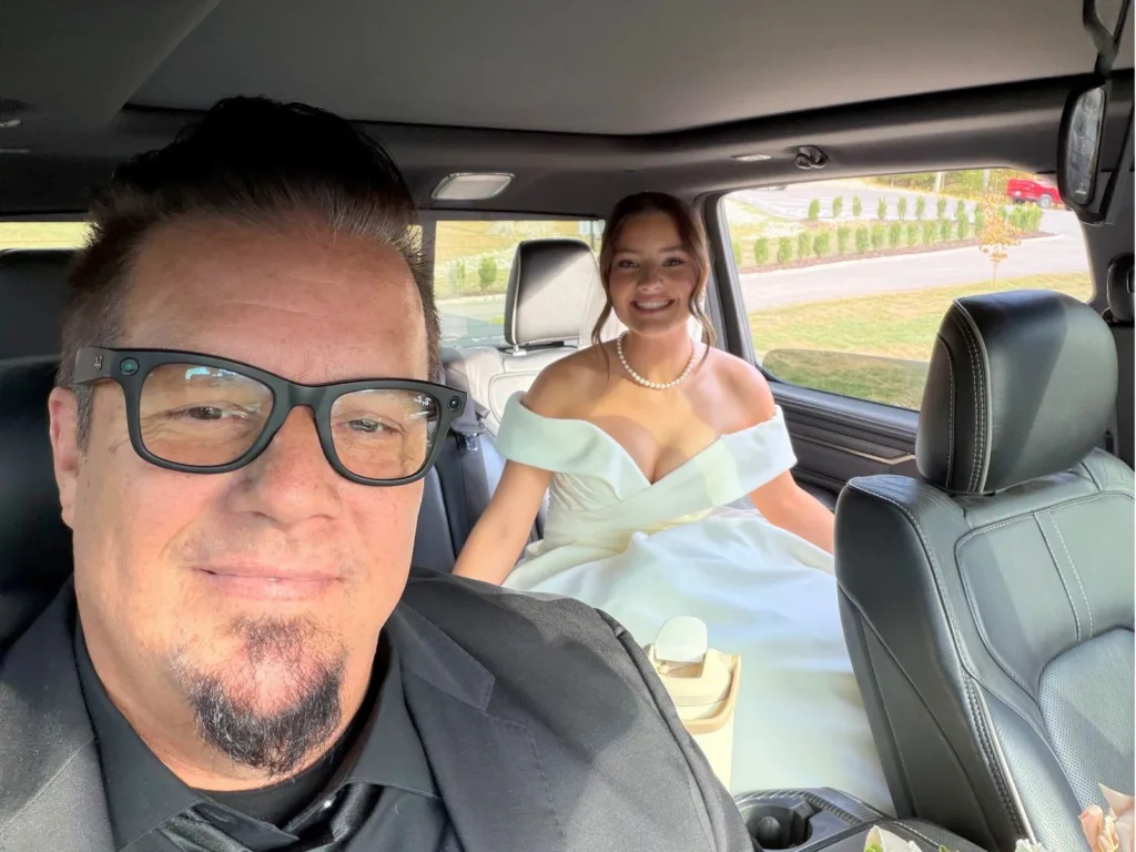 Greg and Madison smile for a selfie inside a car before the wedding ceremony with Madison wearing her bridal gown.