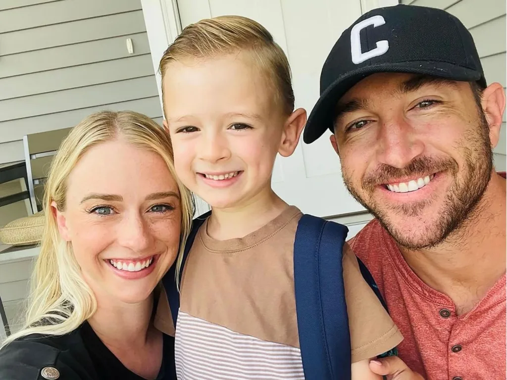 Lexie, Levi, and Josh smile together in a family selfie outside a house, with Levi wearing a backpack.