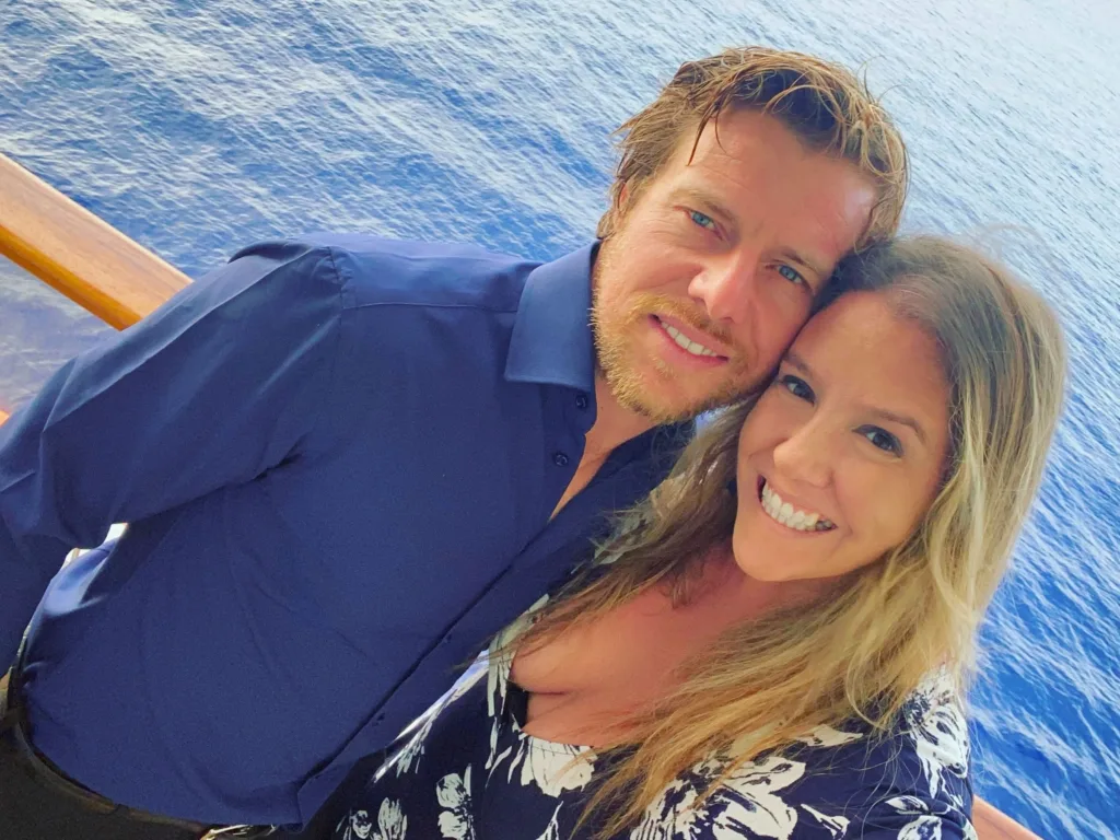 Adrian and Kelly smiling together by the water while taking a selfie.