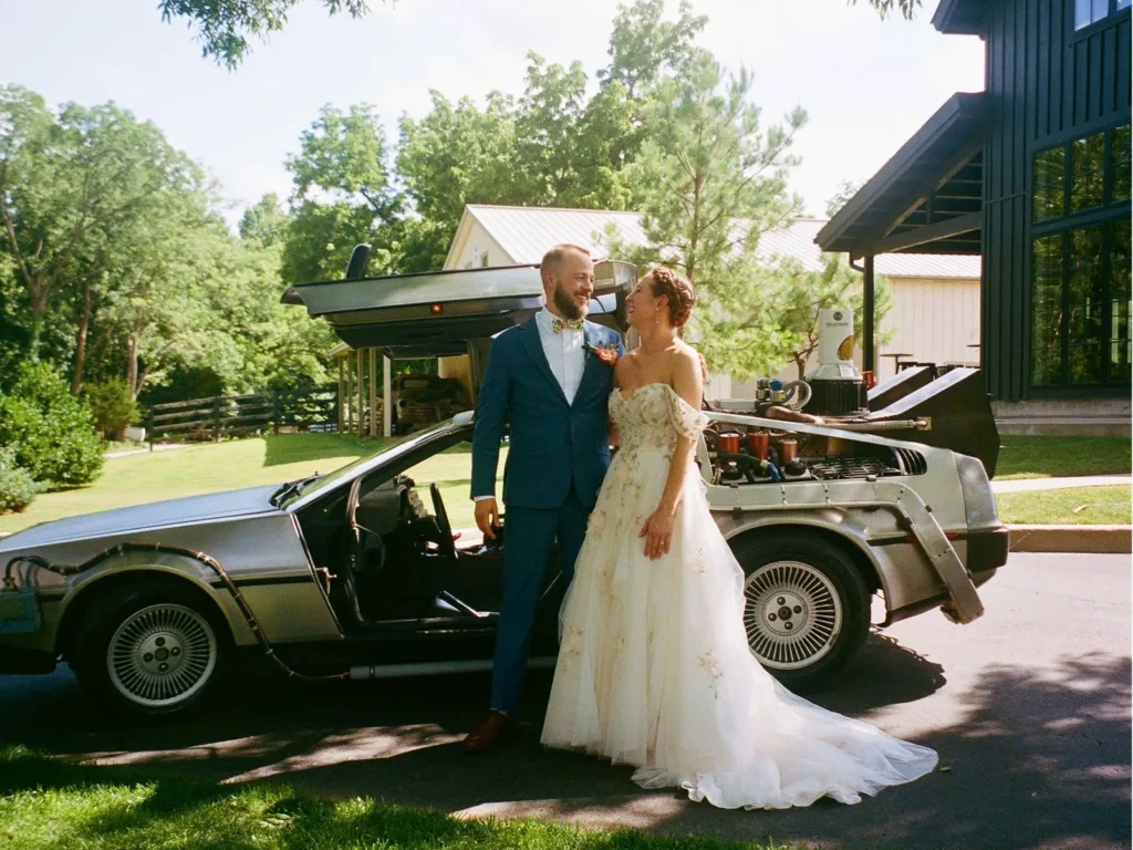 Chris and Emilee stand smiling beside a Back to the Future DeLorean at their wedding venue