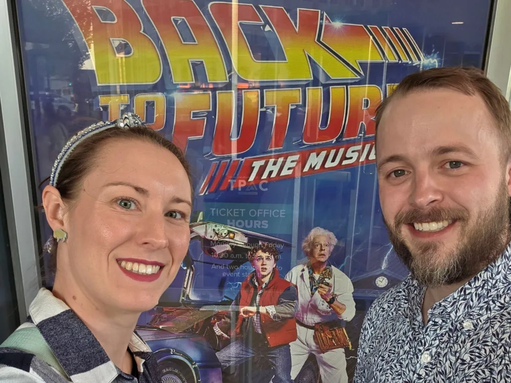 Chris and Emilee stand together in front of a Back to the Future musical poster