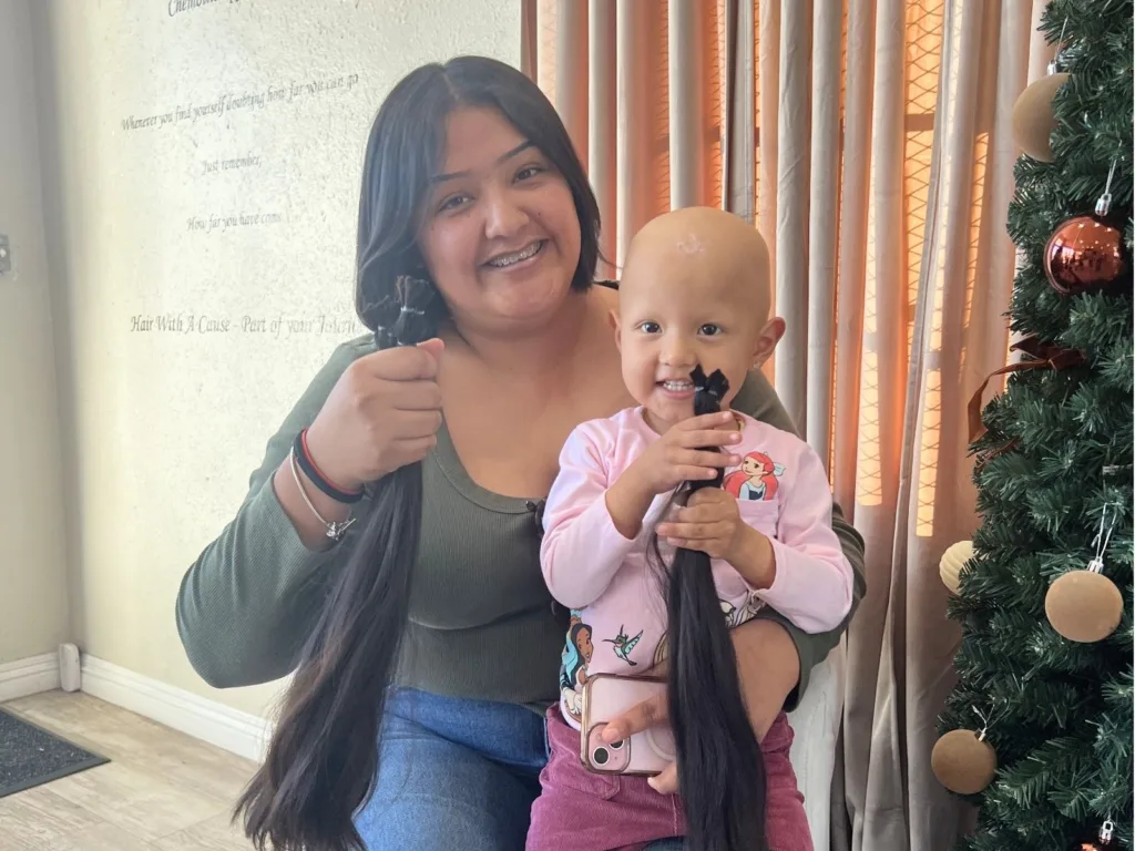 Rubi and Lorelai smile together holding freshly cut hair inside their home.