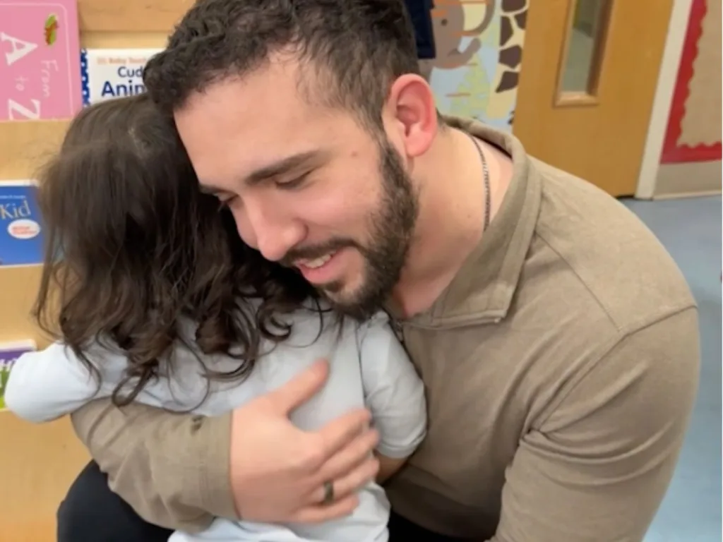 Ian crouches down and hugs Esme tightly inside her classroom during their emotional reunion